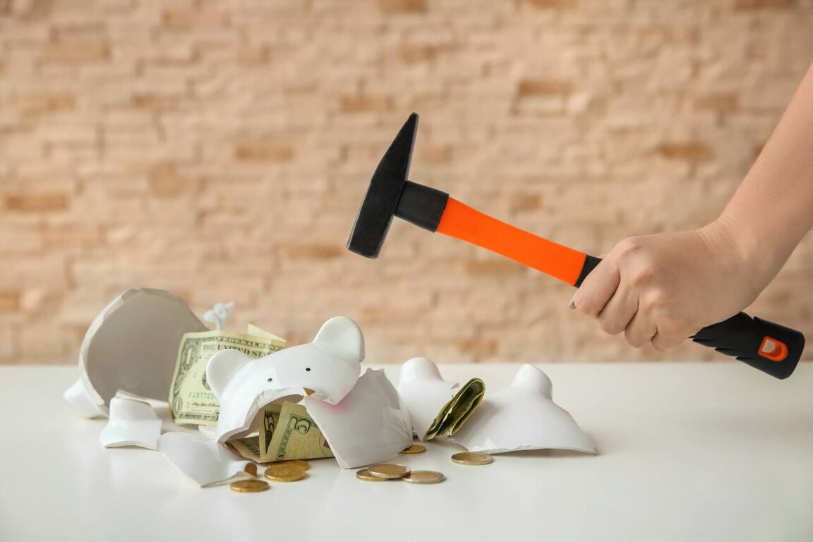 Woman with hammer near broken piggy bank indoors